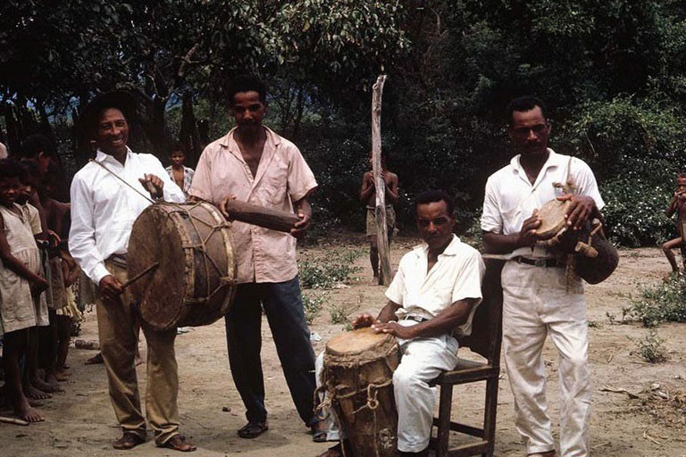 四个被称为conjunto de caña de millo的人在一片贫瘠的土地和郁郁葱葱的植被中敲着鼓。