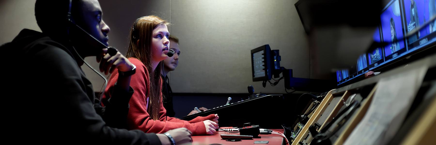 学生坐在幕后电视生产站和在屏幕上观看录像。