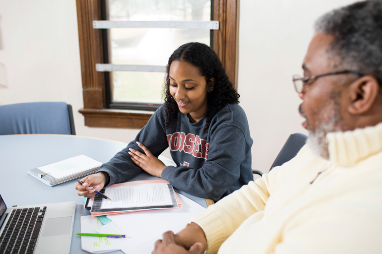 一个年长的男人和一个年轻的女人坐在桌旁。他们正在一起看文件。